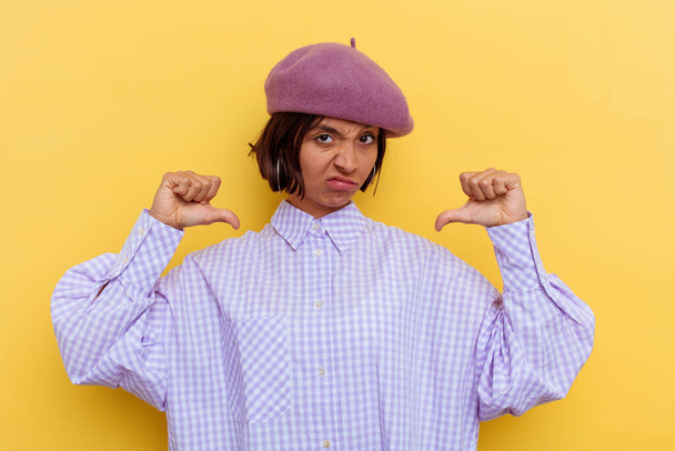 Młoda mieszana kobieta rasy nosi beret odizolowany na żółtym tle czuje dumę i pewność siebie, przykład do naśladowania. - Zdjęcie, obraz