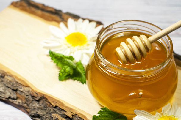 Свежий мед в банке на деревянном бревне с маргаритками - Фото, изображение