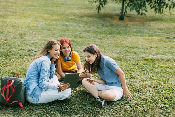 Teinitytöt istuvat puistossa vihreällä nurmikolla tauon aikana. Koulutus ja tieto, teini-ikäisten elämäntapa - Valokuva, kuva