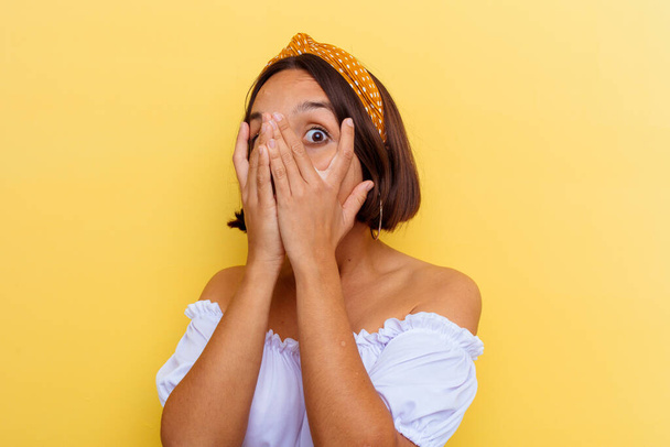 Young mixed race woman isolated on yellow background blink through fingers frightened and nervous. - 写真・画像