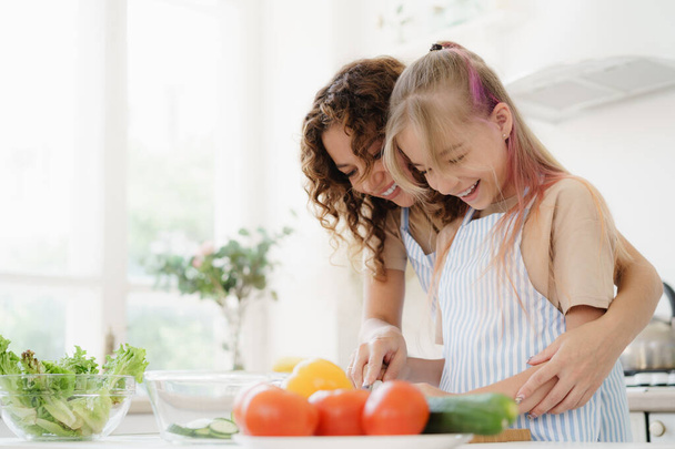 Mother and teen daughter preparing vegetable salad at kitchen - Photo, Image