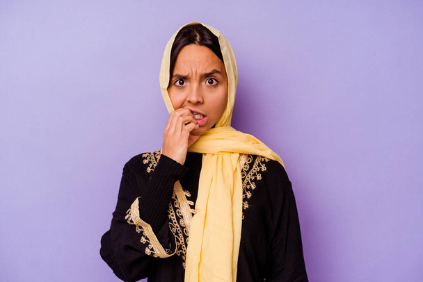 Молодая арабская женщина в типичном арабском костюме, изолированная на фиолетовом фоне, кусающая ногти, нервная и очень беспокойная.. - Фото, изображение