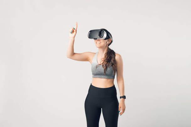 Молода спортивна жінка носить деякі окуляри VR та спортивний одяг на білому тлі. Діяльність через концепцію віртуальної реальності
. - Фото, зображення