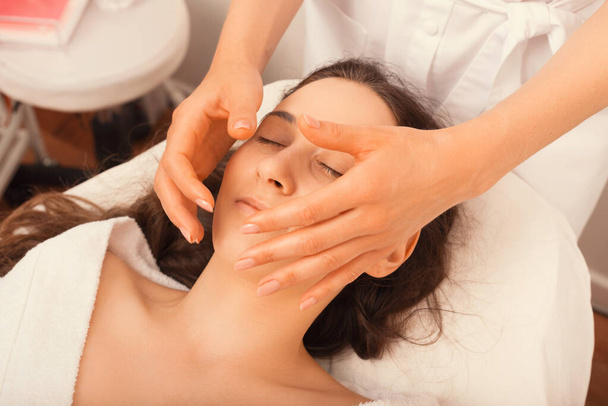 Досить молода жінка насолоджується масажем обличчя у косметолога, лежачи і відпочиваючи
. - Фото, зображення