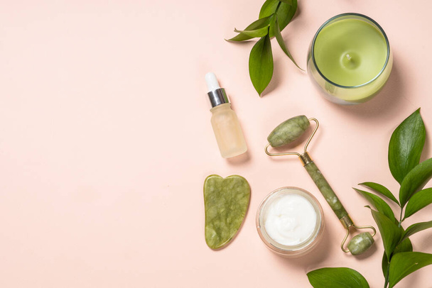 Cosmetic products - Jade roller and gua sha massager with cream and serum bottles at pastel background. - Foto, Imagen