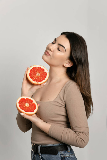 Profiel portret van een jonge vrouw met een perfecte huid en haar, met in de handen een grapefruit geïsoleerd op beige achtergrond studio portret. Begrip "dieetprocedures voor de gezondheidszorg". - Foto, afbeelding