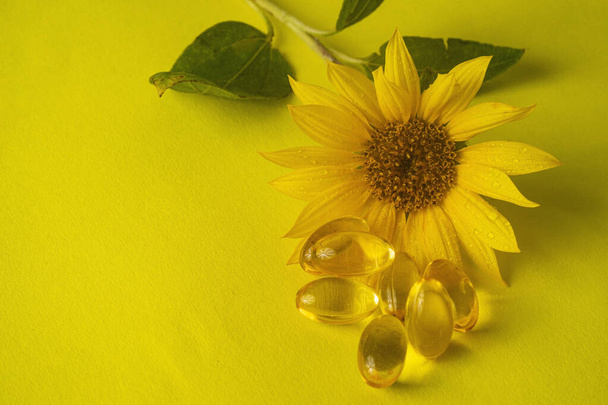 oil pills and a sunflower on yellow background - Foto, Imagen