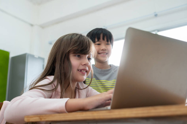 Diverse Multi ethnic of students with Education and E-Learning technology. Caucasian girl and Asian boy enjoying using laptop for learning in classroom at primary school. - Foto, imagen