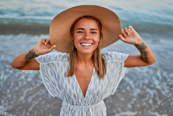 Una donna carina in un cappello di paglia e vestito sta riposando vicino al mare e godersi la sua vacanza. - Foto, immagini