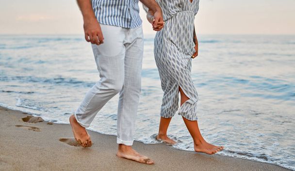 Egy szerelmes fiatal pár sétál a tengerparton kéz a kézben, élvezik egymást és vakációjukat, romantikusan töltenek egy kis időt a parton.. - Fotó, kép