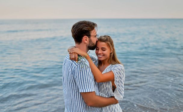 Młoda para w miłosnym uścisku nad brzegiem morza, romantycznie spędza czas ciesząc się sobą i wakacjami. - Zdjęcie, obraz