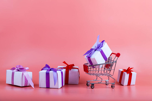 Shopping cart and gifts on a pink background. Concept: buying gifts. - Foto, imagen