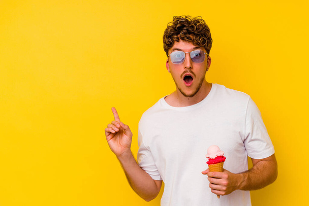 Молодий білий чоловік їсть морозиво ізольовано на жовтому тлі, вказуючи на бік
 - Фото, зображення