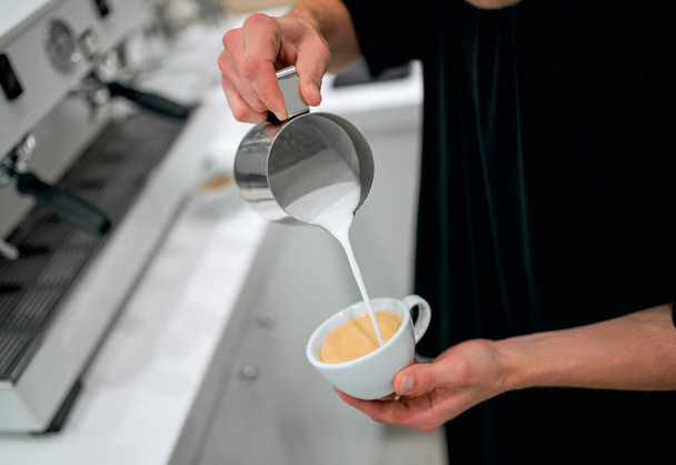 Επαγγελματίας barista ρίχνει ατμό γάλα σε φλιτζάνι καφέ στην καφετέρια. - Φωτογραφία, εικόνα
