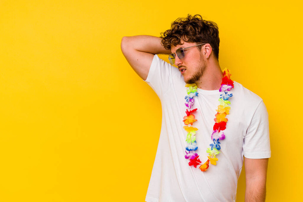 Junger kaukasischer Mann in einem Hawaiihemd auf gelbem Hintergrund, der den Hinterkopf berührt, nachdenkt und eine Wahl trifft. - Foto, Bild