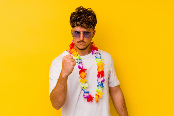 カメラに拳を示す黄色の背景に隔離されたハワイのパーティーのものを身に着けている若い白人男性,積極的な表情. - 写真・画像