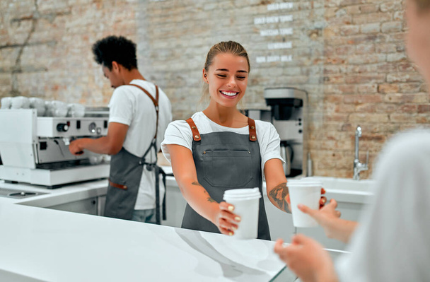 Blanke aantrekkelijke vrouw barista het geven van kopjes koffie, latte of cappuccino aan de klant in de coffeeshop. - Foto, afbeelding