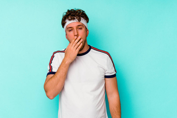 Jovem homem caucasiano esporte isolado no fundo azul bocejo mostrando um gesto cansado cobrindo a boca com a mão. - Foto, Imagem