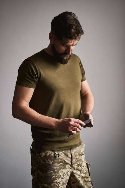 Strong military man sharpening his pocket knife with a whetstone - Foto, imagen
