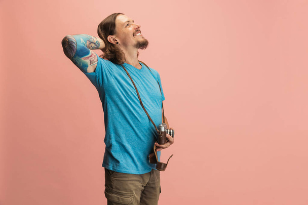 Young man, photographer, cameraman standing and dreaming isolated on pink studio background. Concept of occupation, job, funny meme emotions - Foto, imagen