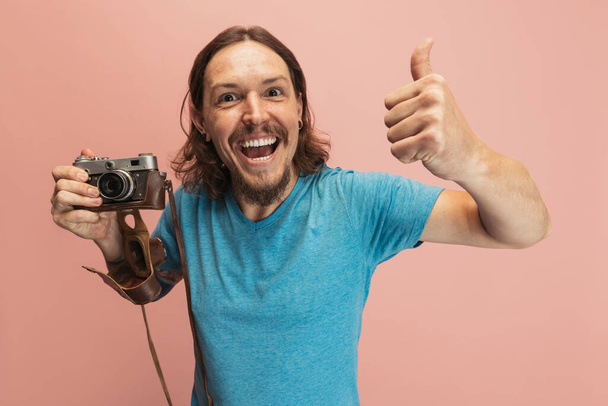 Portrait of young man, photographer, cameraman with retro camera isolated on pink studio background. Concept of occupation, job, funny meme emotions - Foto, immagini