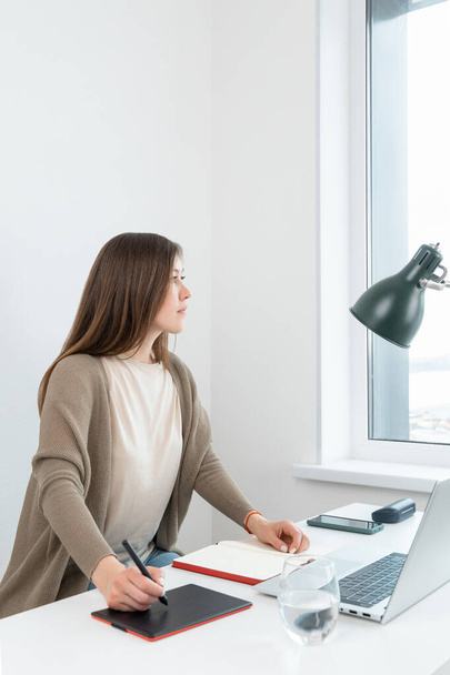 Przemyślana kobieta siedząca przy stole z laptopem i odwracająca wzrok. Biała kobieta grafik myśli o rozwiązaniu problemu w pracy. Rozważanie decyzji, podejmowanie ważnych decyzji. - Zdjęcie, obraz
