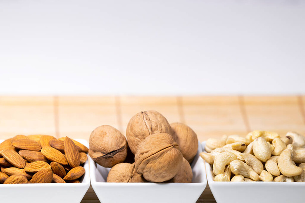 Pähkinät, Manteli, cashew, Wallnut valkoisissa keraamisissa kulhoissa puinen jalusta, Terveellinen välipala ruoka, Ruokavalio, Trendikäs ateria - Valokuva, kuva
