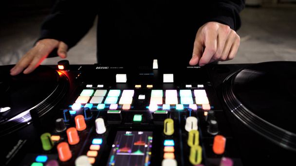 Detailní záběr DJ pomocí moderního mixéru pro přehrávání elektrohudby v nočním klubu. Umění. Barevné tlačítka a vinyl, vybavení DJ. - Fotografie, Obrázek