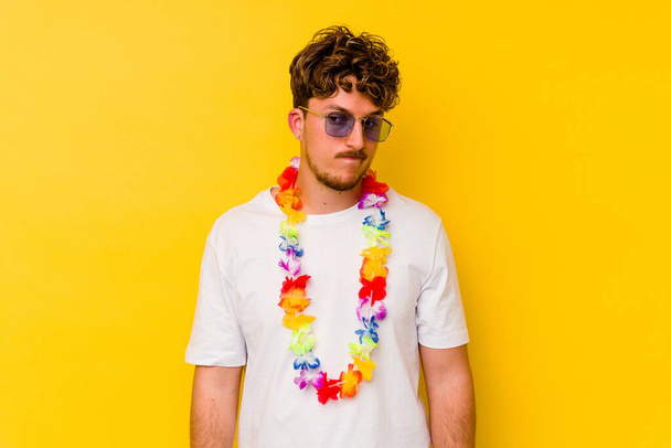 Jovem caucasiano vestindo uma festa havaiana coisas isoladas em fundo amarelo confuso, se sente duvidoso e inseguro. - Foto, Imagem