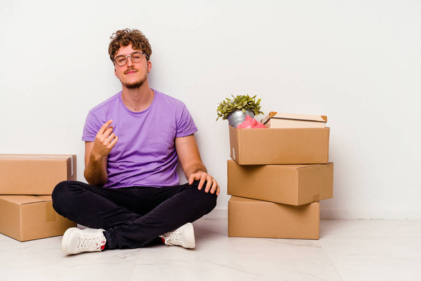 Young caucasian man sitting on the floor ready for moving isolated on white background pointing with finger at you as if inviting come closer. - Photo, Image