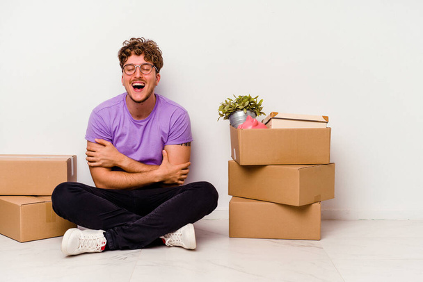 Young caucasian man sitting on the floor ready for moving isolated on white background laughing and having fun. - Photo, Image