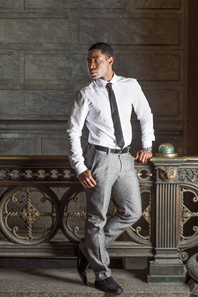 In weißem Hemd, schwarzer Krawatte, grauer Hose steht ein junger, gutaussehender, schwarzer Geschäftsmann an einem Geländer und wartet auf sein Geld. - Foto, Bild