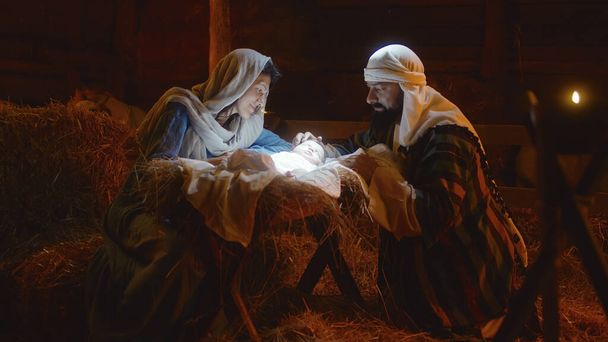 Maryja i Józef pieszczą Dzieciątko Jezus w oświetlonym żłobie - Zdjęcie, obraz