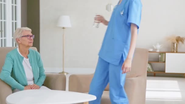 Enfermera da agua mineral a la señora mayor sentada en la mesa - Metraje, vídeo