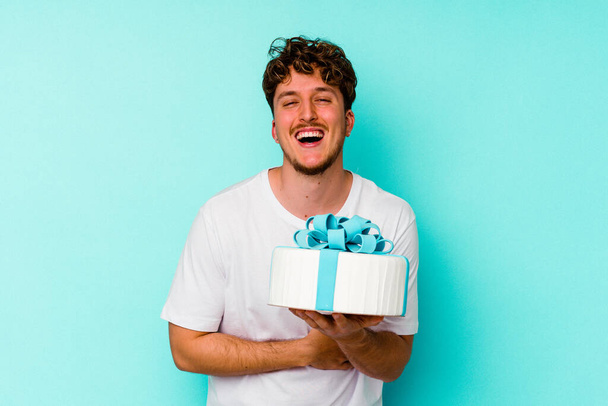 Молодий білий чоловік тримає торт ізольовано на синьому фоні сміється і розважається
. - Фото, зображення