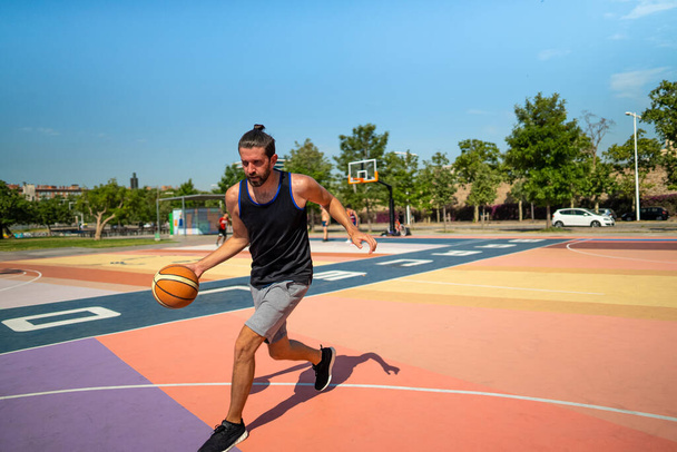 Een mannelijke basketbalspeler loopt op een basketbalveld met een bal - Foto, afbeelding