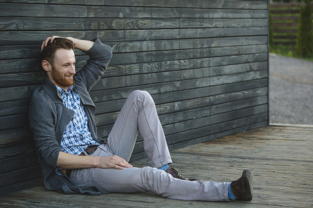 Красивий молодий чоловік сидить на дерев'яній підлозі
 - Фото, зображення