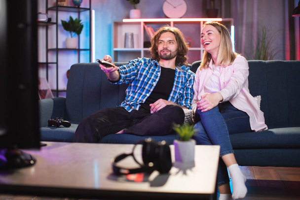 Caucasian couple sitting together on the sofa at home, watching TV, and having fun - Valokuva, kuva