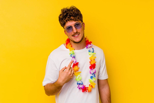 Junger kaukasischer Mann in einem Hawaiihemd auf gelbem Hintergrund, der mit dem Finger auf dich zeigt, als würde er dich einladen, näher zu kommen. - Foto, Bild