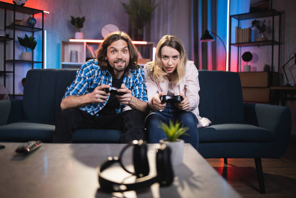 Kaukasisches Paar sitzt abends zu Hause und spielt Videospiele am Fernseher mit Steuerknüppel - Foto, Bild
