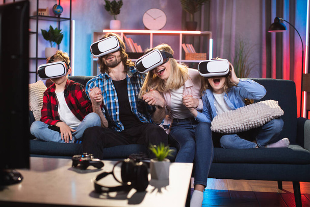 Family sitting on the sofa at home in the evening and using virtual reality headsets - Photo, Image