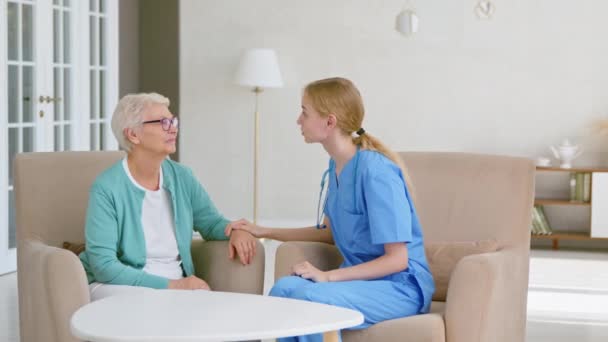 Blonde doctor talks cheering up senior woman in light office - Záběry, video
