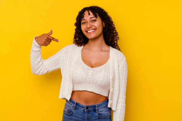 Jonge gemengde ras vrouw geïsoleerd op gele achtergrond persoon wijzend met de hand naar een shirt kopieerruimte, trots en zelfverzekerd - Foto, afbeelding