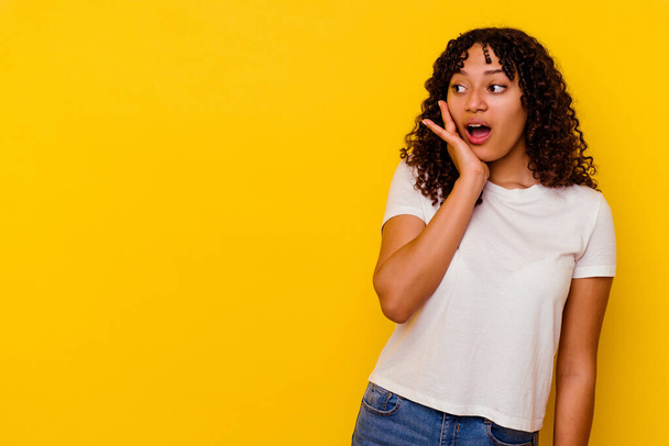 Young mixed race woman isolated on yellow background being shocked because of something she has seen. - Foto, imagen