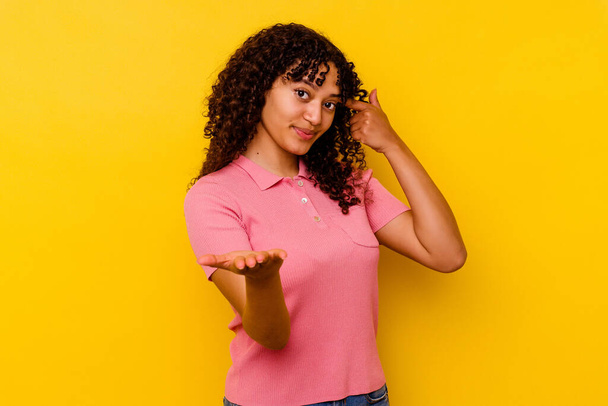 Jeune femme métisse isolée sur fond jaune tenant et montrant un produit à portée de main. - Photo, image