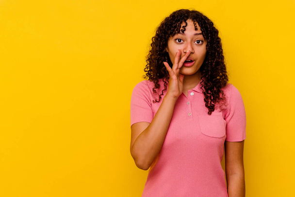Young mixed race woman isolated on yellow background is saying a secret hot braking news and looking aside - Photo, Image