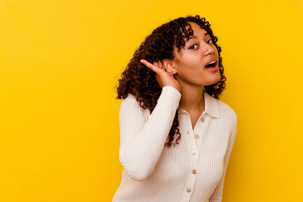 Young mixed race woman isolated on yellow background trying to listening a gossip. - Foto, Imagem