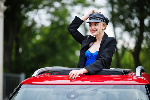 Portrait of beautiful blonde sexy fashion woman model in cap and in all black with bright makeup in red city car open sunroof. - Valokuva, kuva