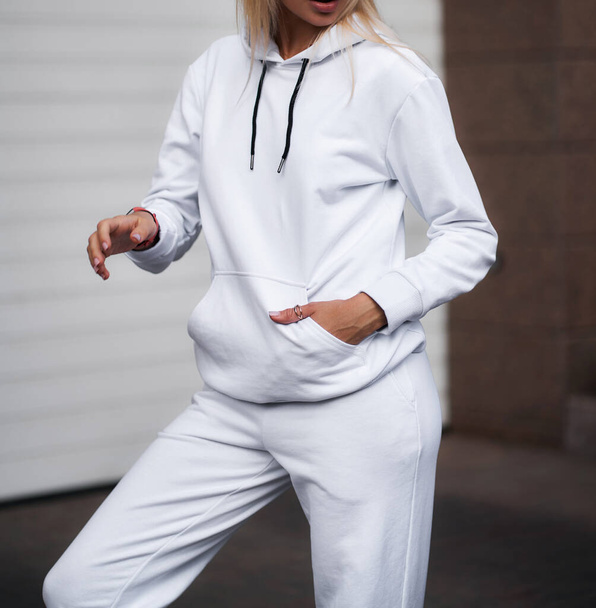voor meisje draagt witte hoodie en broek. Blondine vrouw in los trainingspak zonder logo - Foto, afbeelding