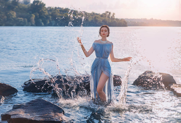Greek mythical fairytale fantasy woman goddess nymph emerges from lake. Splashes of water. Vintage blue long sexy wet dress. summer nature forest, water surface of river coastal stones. Girl mermaid - Foto, Imagem